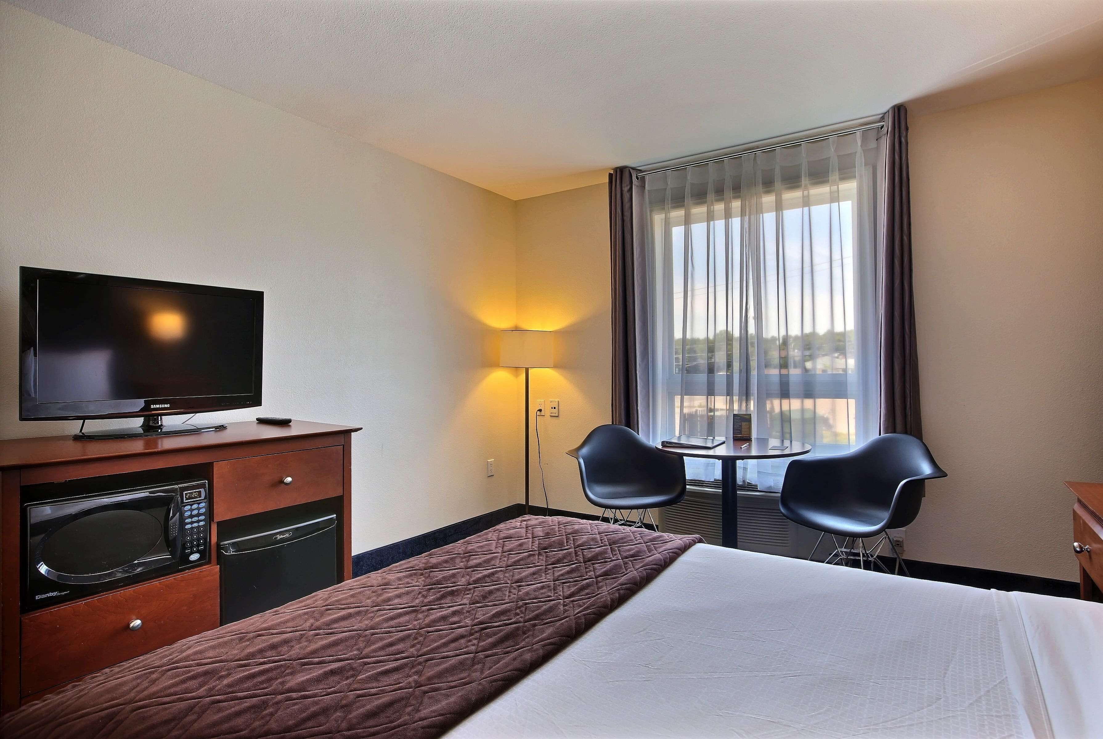 A hotel room with a bed, a television, a microwave, a small table, two chairs, and a window with curtains.