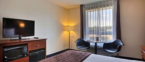A hotel room with a bed, a television, a microwave, a small table, two chairs, and a window with curtains.
