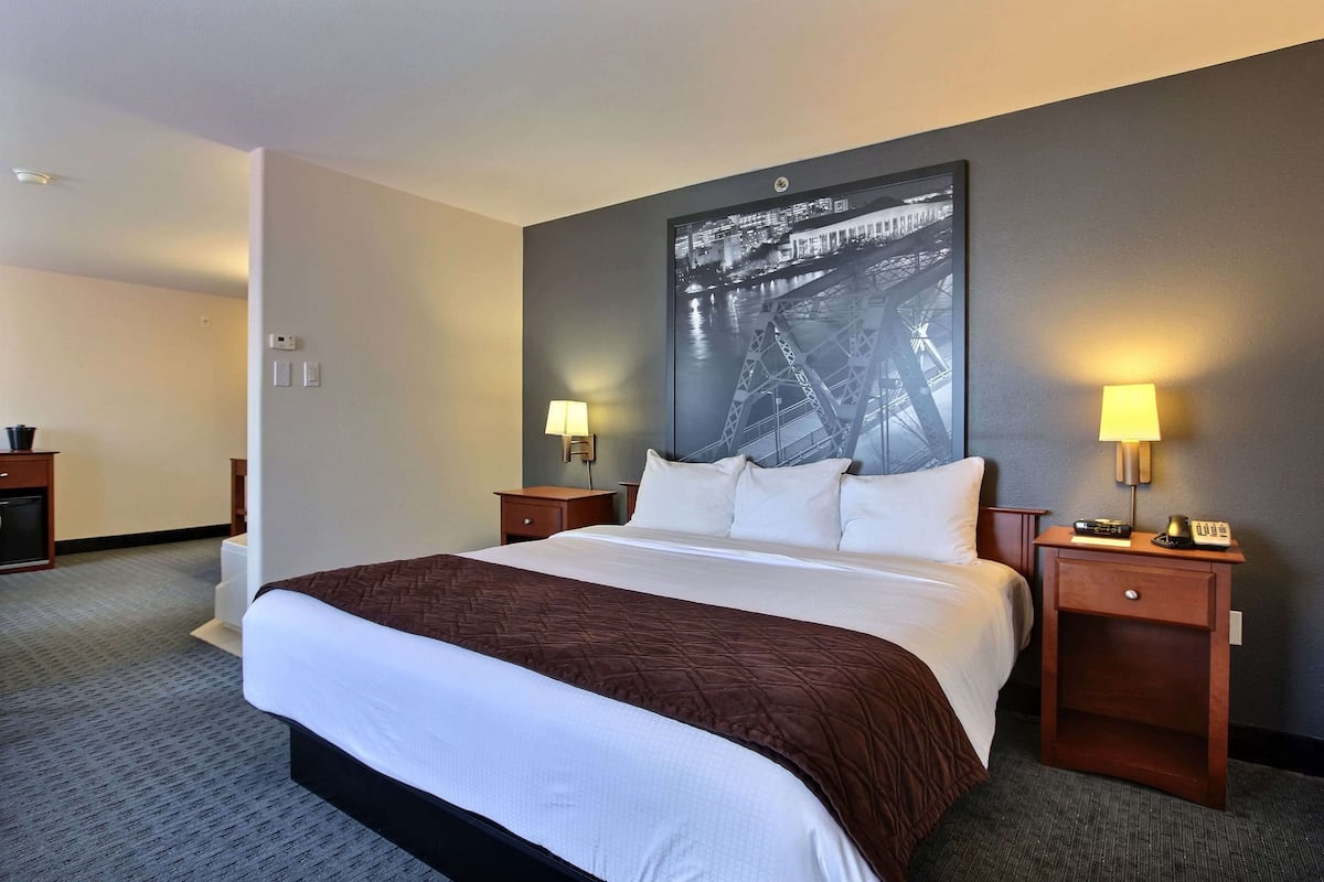 A hotel room with a large bed, two bedside tables with lamps, a wall-mounted picture of a bridge, and a carpeted floor.