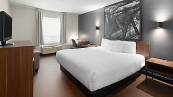 A modern hotel room with a large bed, a desk, a chair, a television, and a large window with curtains.