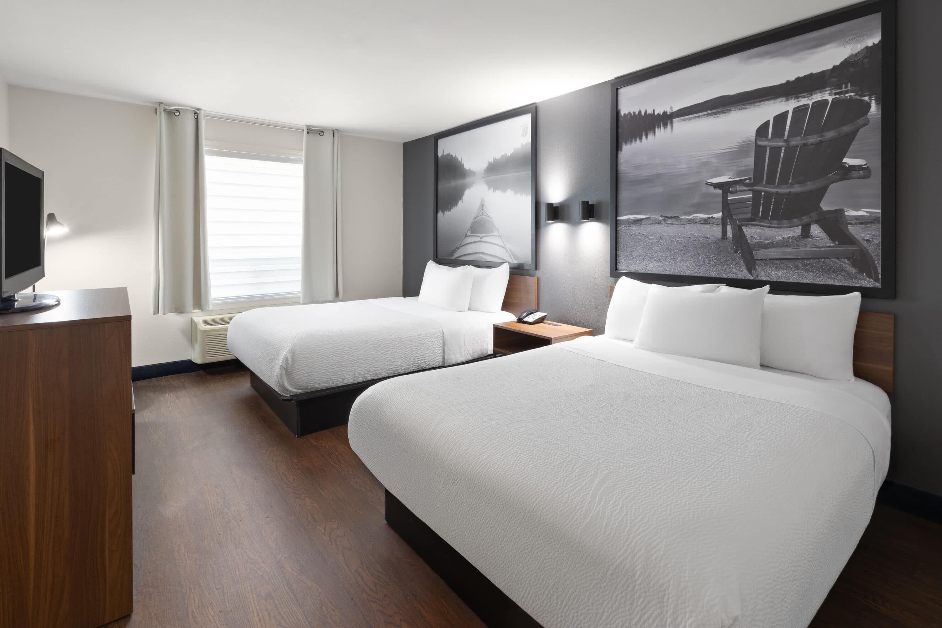 Ein Hotelzimmer mit zwei Betten, einem Fernseher, einem Schreibtisch und Bildern an den Wänden.