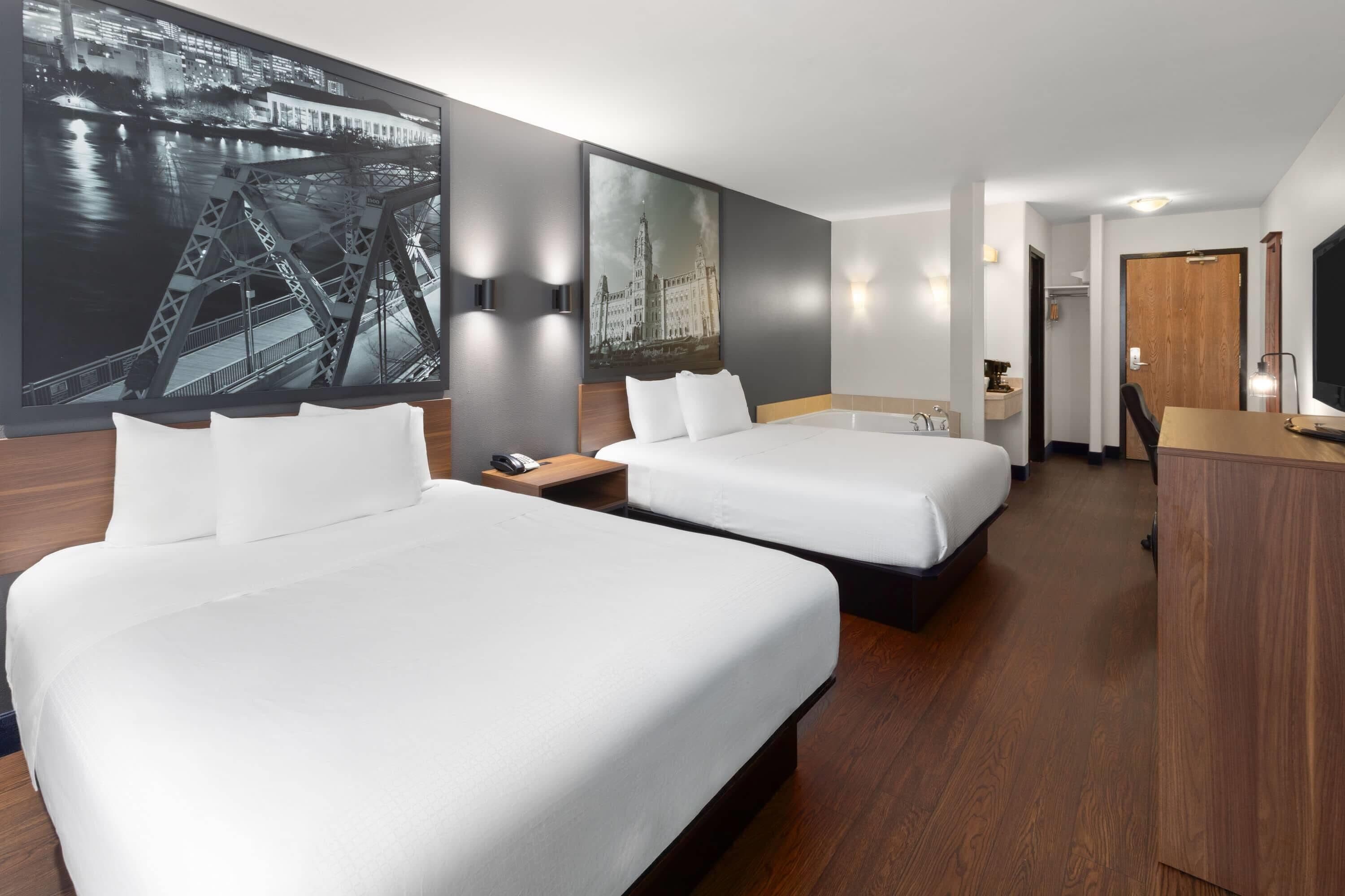 Habitación de hotel con dos camas, un cuadro grande de un paisaje urbano, un escritorio de madera y un televisor.