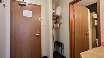A hotel room with a wooden door, a coat rack, a towel rack, and a shower area.