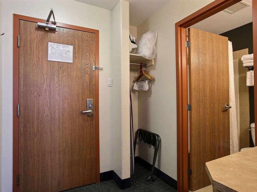 Quarto de hotel com porta de madeira, um cabideiro, porta-toalhas e área de chuveiro.