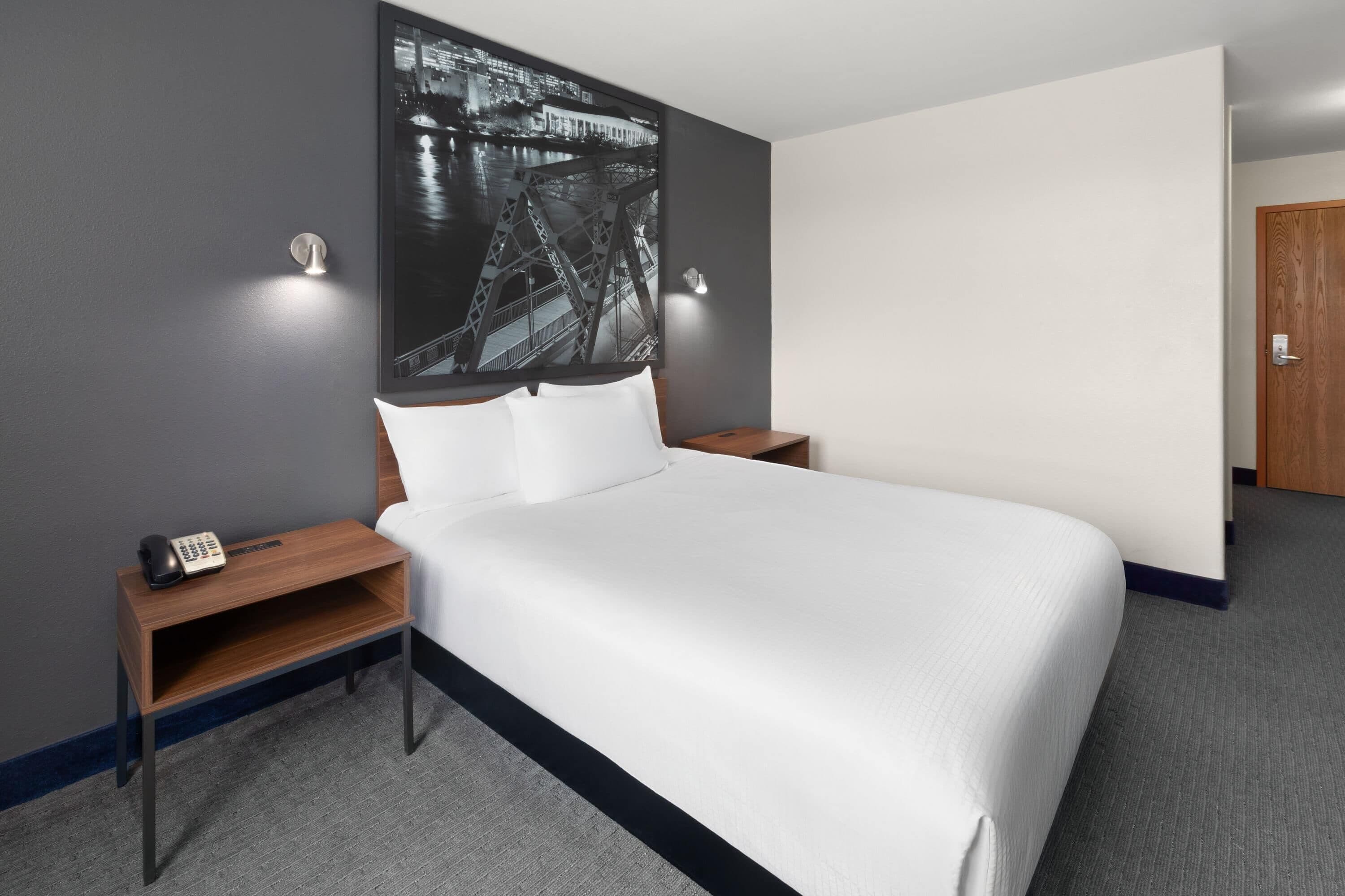 Habitación de hotel con una cama grande, una mesita de noche con teléfono y una lámpara fijada en la pared.