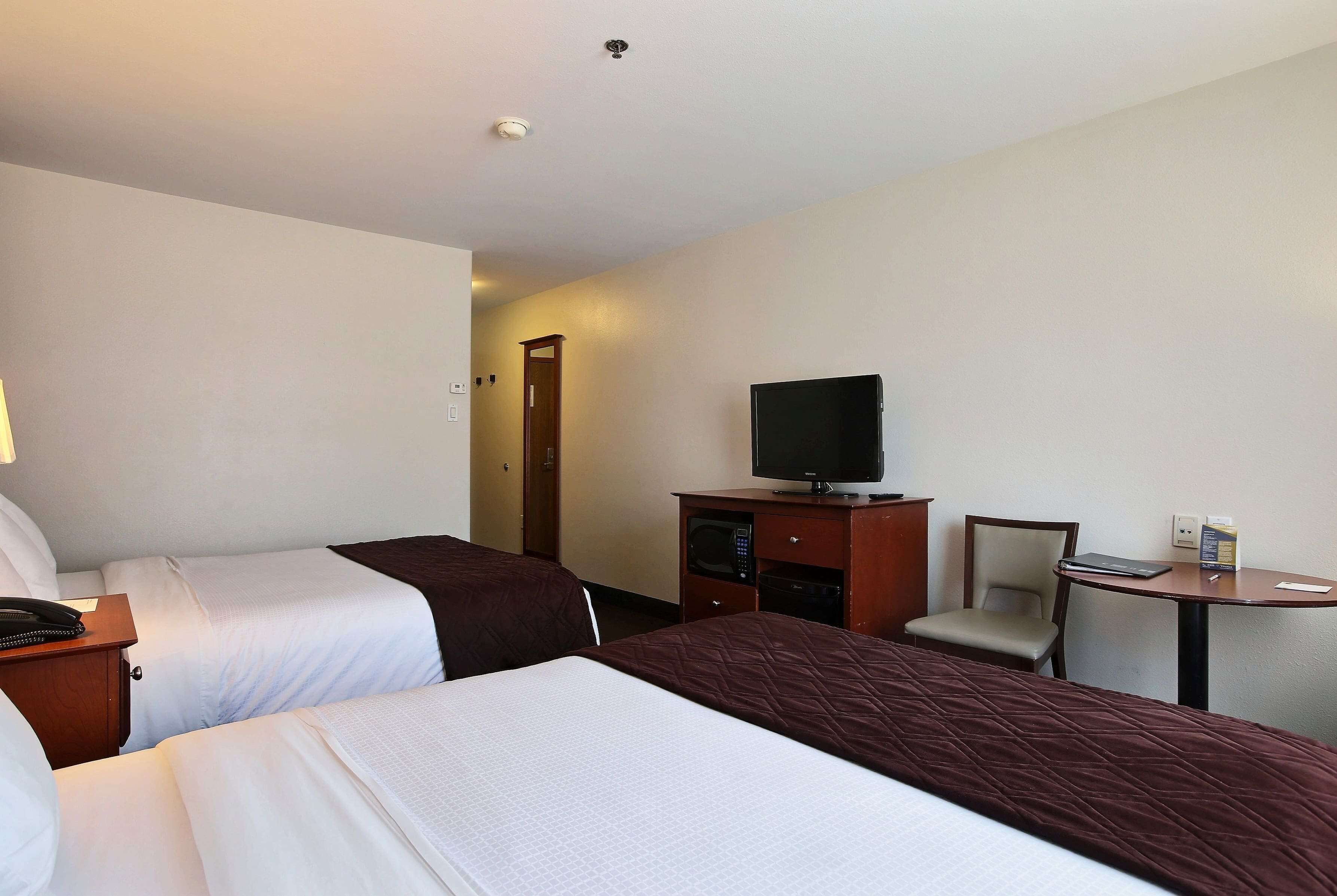 A hotel room with two beds, a television, a desk with a chair, and a microwave.