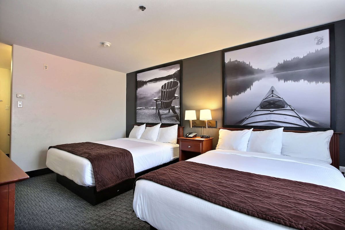 A hotel room with two beds, a desk, and a nightstand with lamps.