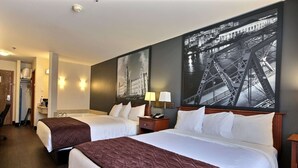 A hotel room with two beds, a nightstand with a lamp, and a large framed picture of a bridge.
