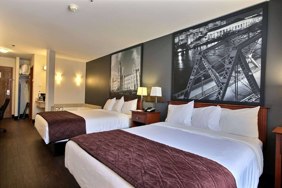 A hotel room with two beds, a nightstand with a lamp, and a large framed picture of a bridge.