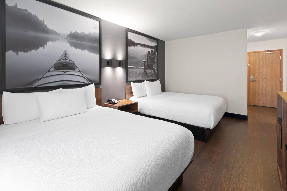 A hotel room with two beds, a wooden floor, and a large wall-mounted artwork of a lake scene.