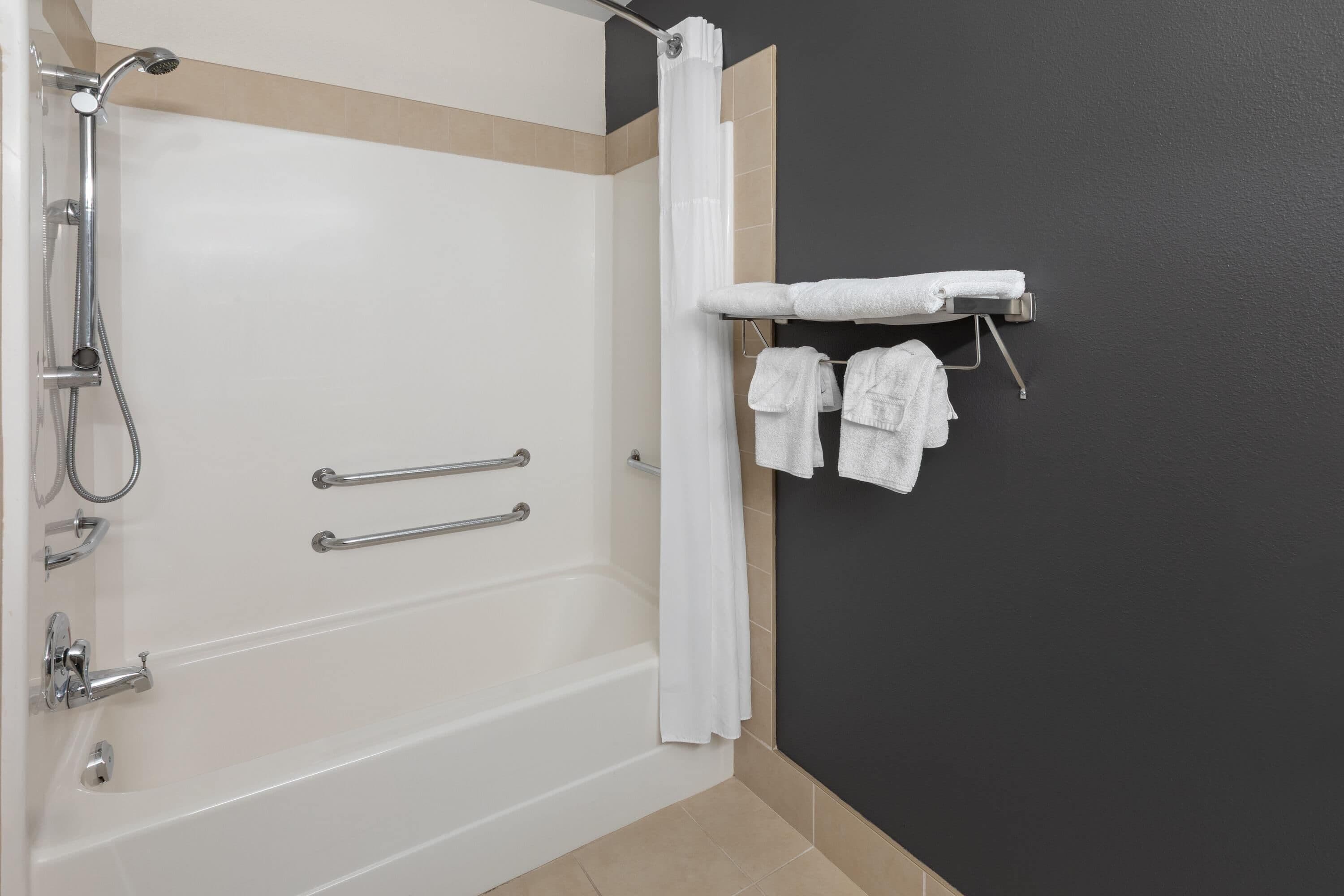 A bathroom with a bathtub, shower, and towel rack with towels.