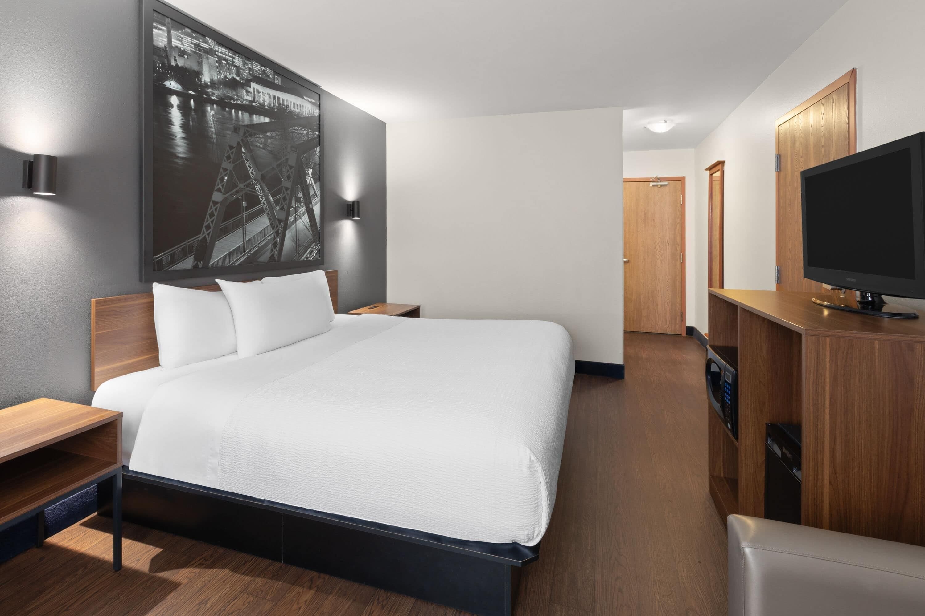 A modern hotel room with a large bed, a flat-screen TV, a wooden cabinet, and a wall-mounted artwork.