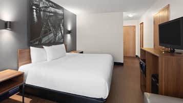 Habitación de hotel moderna con una cama grande, un televisor de pantalla plana, un aparador de madera y una obra de arte colgada en la pared.