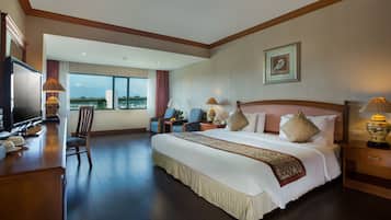 A spacious hotel room with a large bed, a desk with a television, and a view of a bridge through the window.