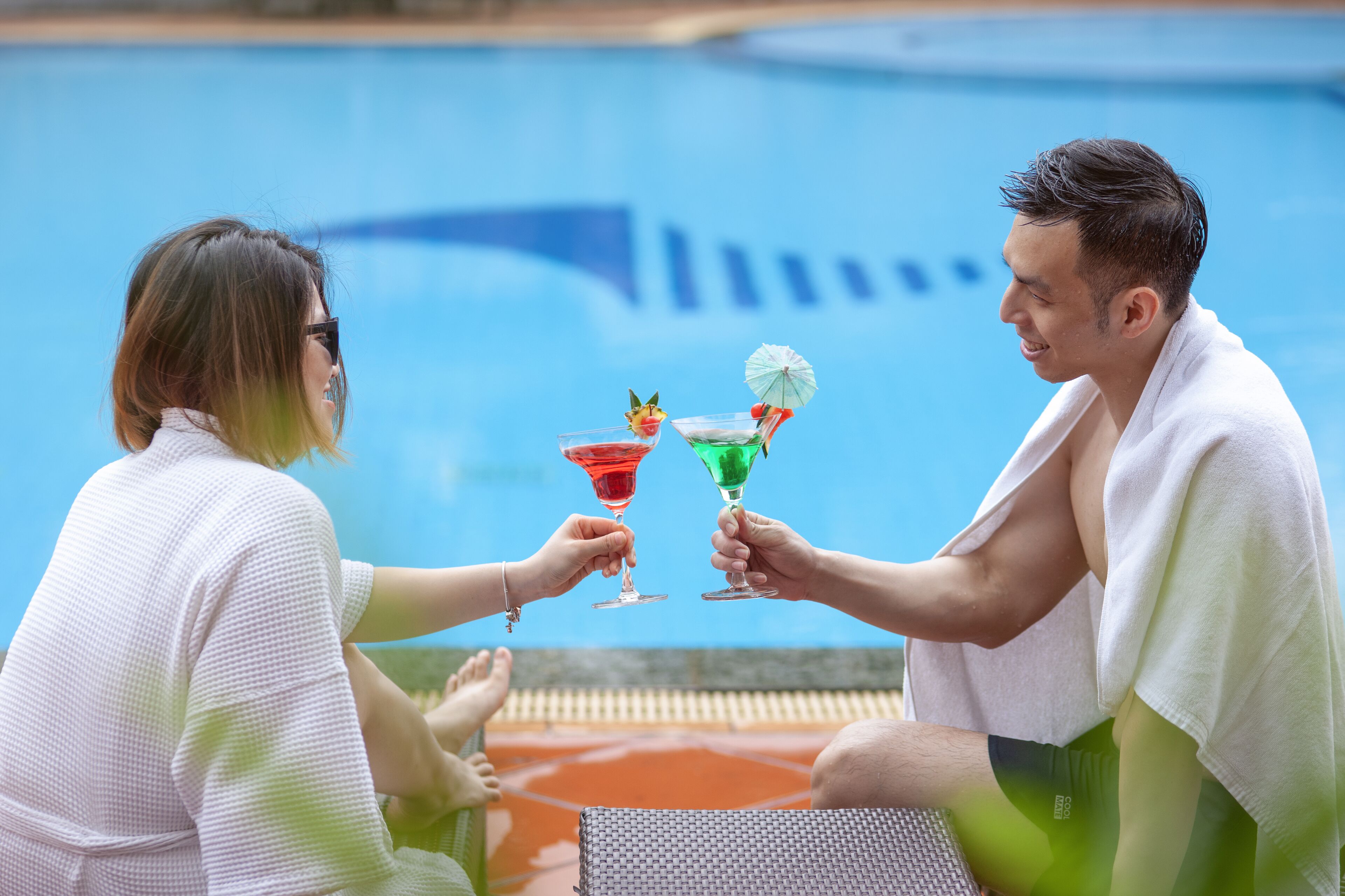 Two people toasting with cocktails by a poolside.