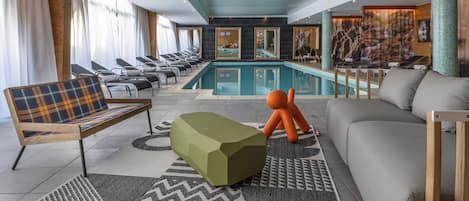 Un espace piscine intérieur moderne, comprenant une piscine, des chaises longues et un canapé.