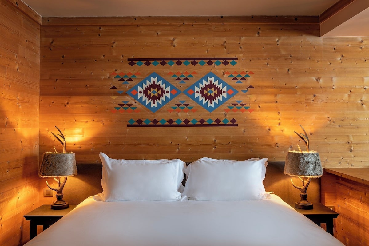 A wooden-paneled room with a bed, two lamps, and a geometric wall decoration.
