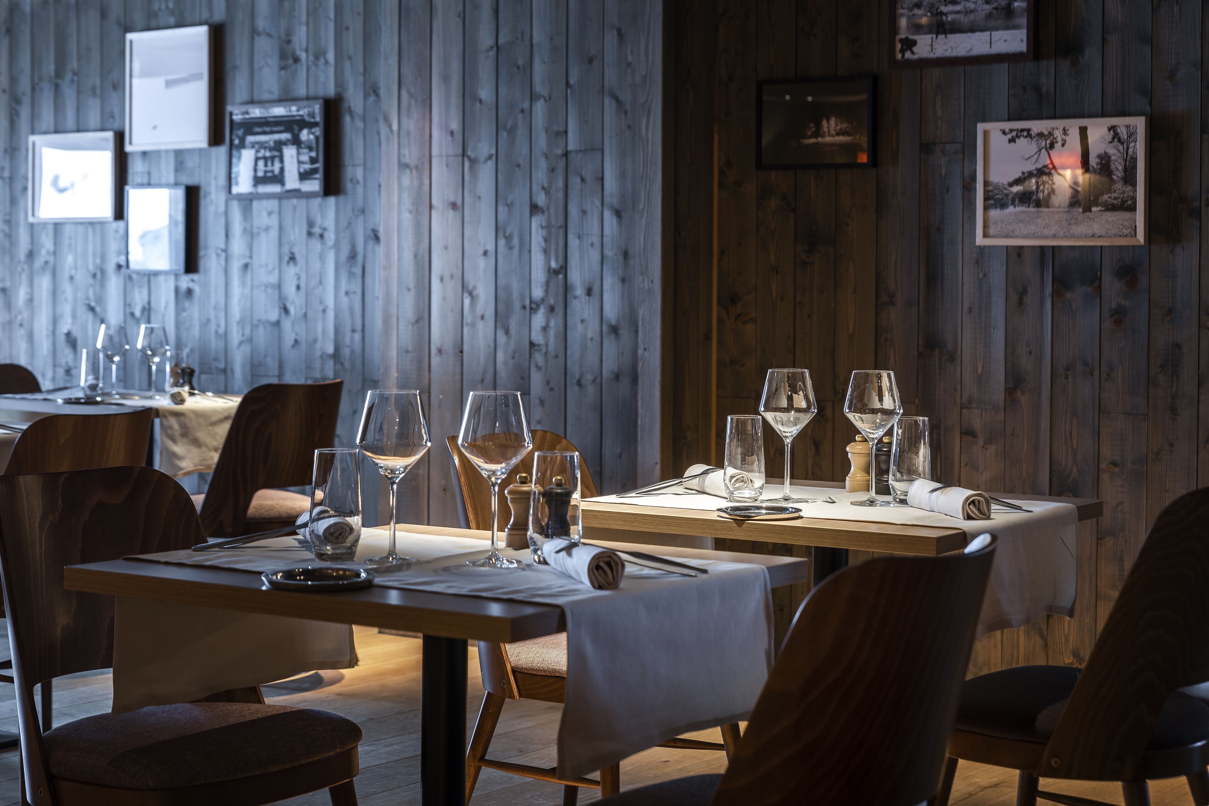 Un restaurante con paredes de madera, mesas dispuestas con copas de vino y platos, y cuadros enmarcados en la pared.