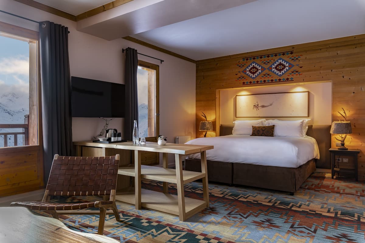 A hotel room with a bed, a desk, a chair, a TV, and a patterned carpet.