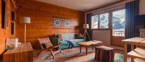 Une pièce chaleureuse avec des murs en bois, un tapis à motifs, un canapé, une table basse et un téléviseur.