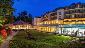 A hotel with a glass-enclosed pool, outdoor seating, and a well-lit facade. - Dorint Seehotel Binz-Therme Binz/Rügen (Binz)