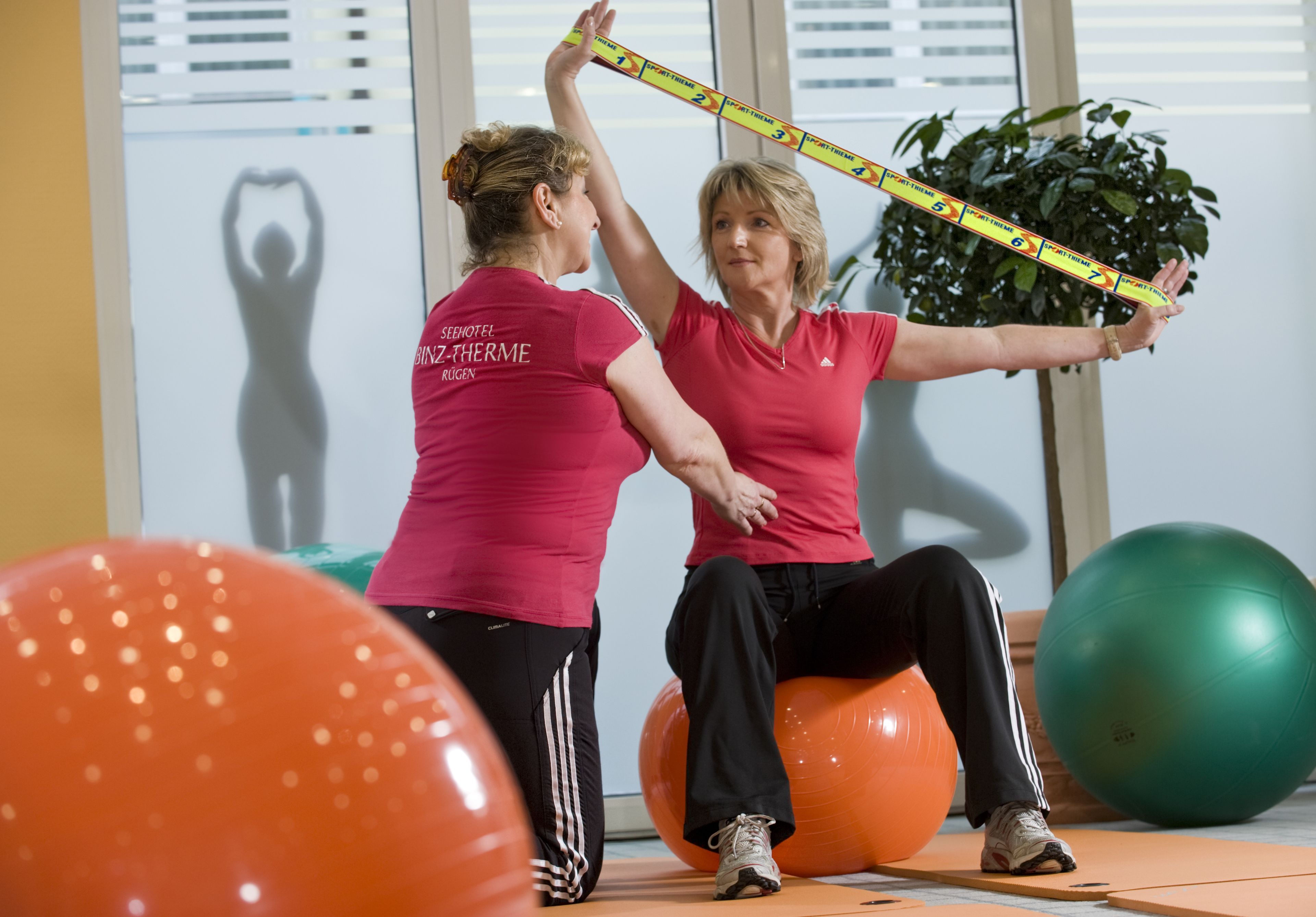Two individuals in a room with exercise equipment, including large exercise balls and a measuring tape.