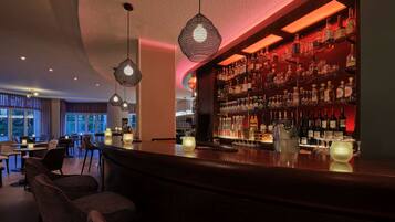 A bar area with a curved counter, hanging pendant lights, and a wall of liquor bottles.