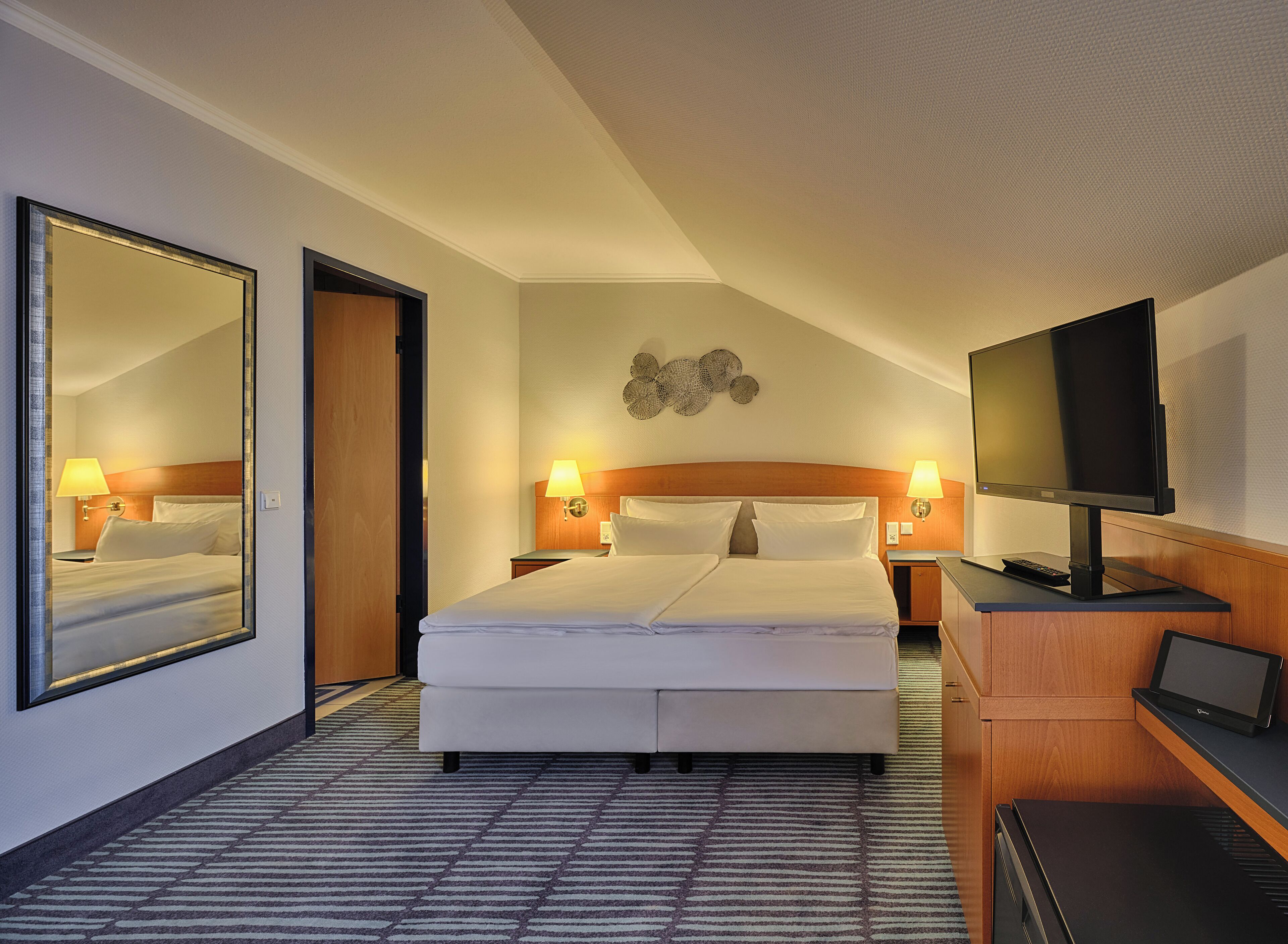 Une chambre d’hôtel avec un grand lit, une télévision, un bureau avec un ordinateur portable et un miroir.