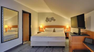 A hotel room with a large bed, a TV, a desk with a laptop, and a mirror.