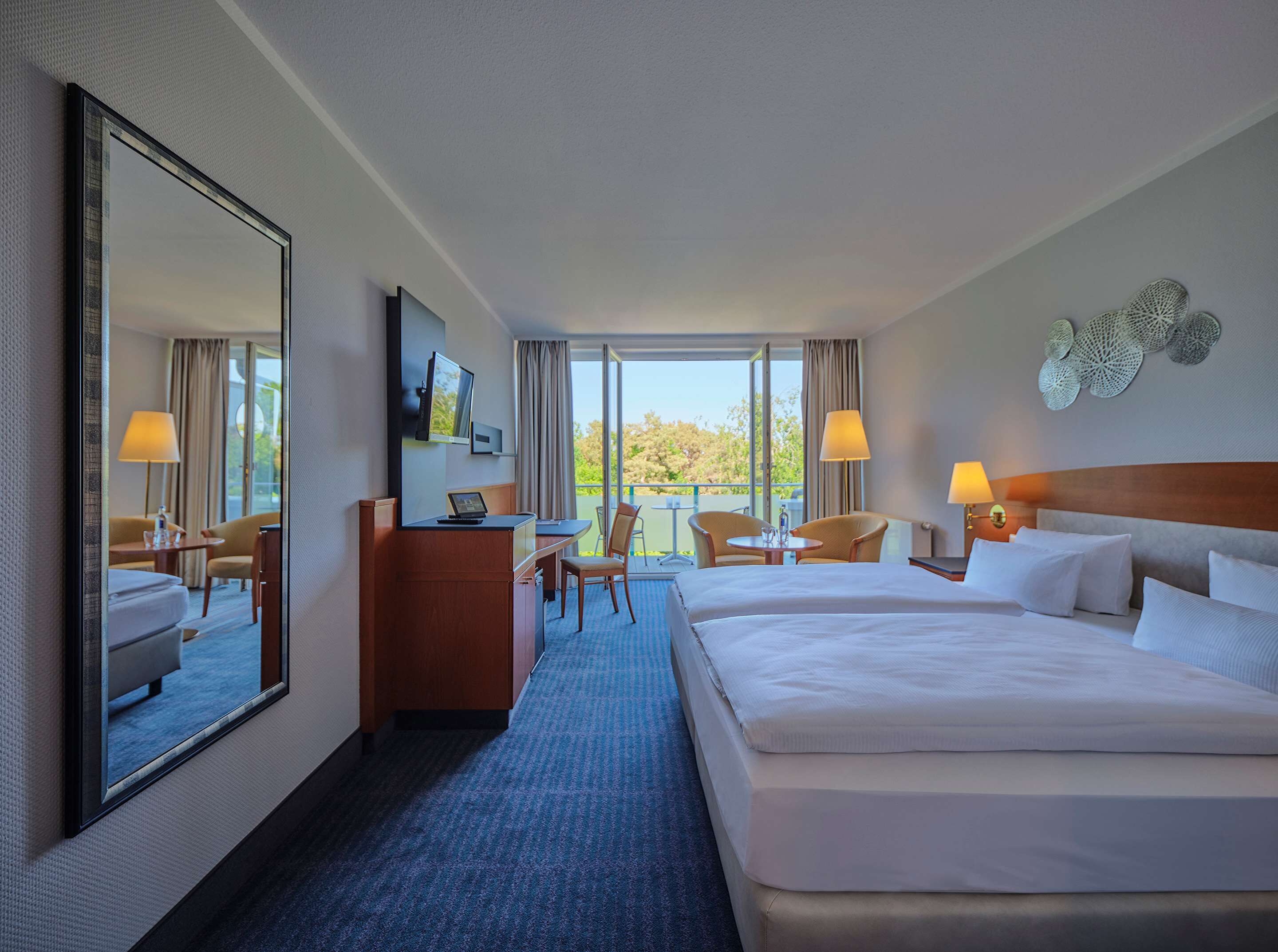 A hotel room with a large bed, a desk, a chair, a TV, and a balcony with a view.