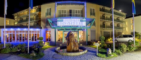 Een hotel met een opvallend bord, een fontein en een auto die er geparkeerd staat.