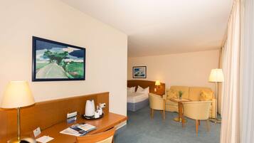 A hotel room with a desk, a chair, a bed, a sofa, and a small table.