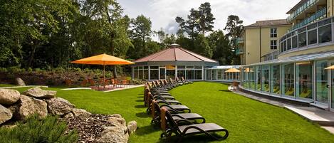 A well-maintained outdoor area with a row of lounge chairs and a gazebo, surrounded by greenery and a building with large windows.