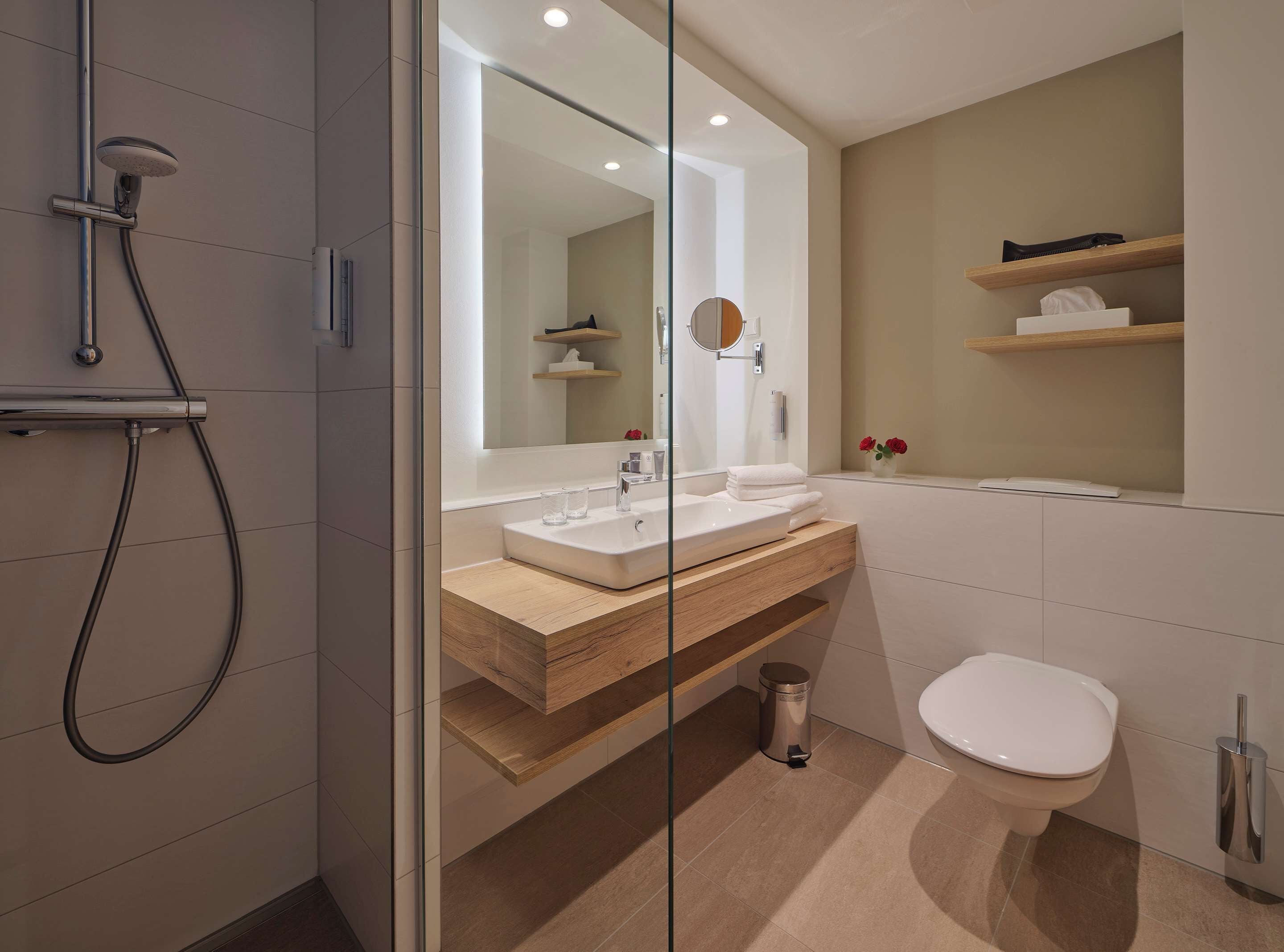 A modern bathroom with a glass shower enclosure, a wooden vanity, a white sink, and a toilet.