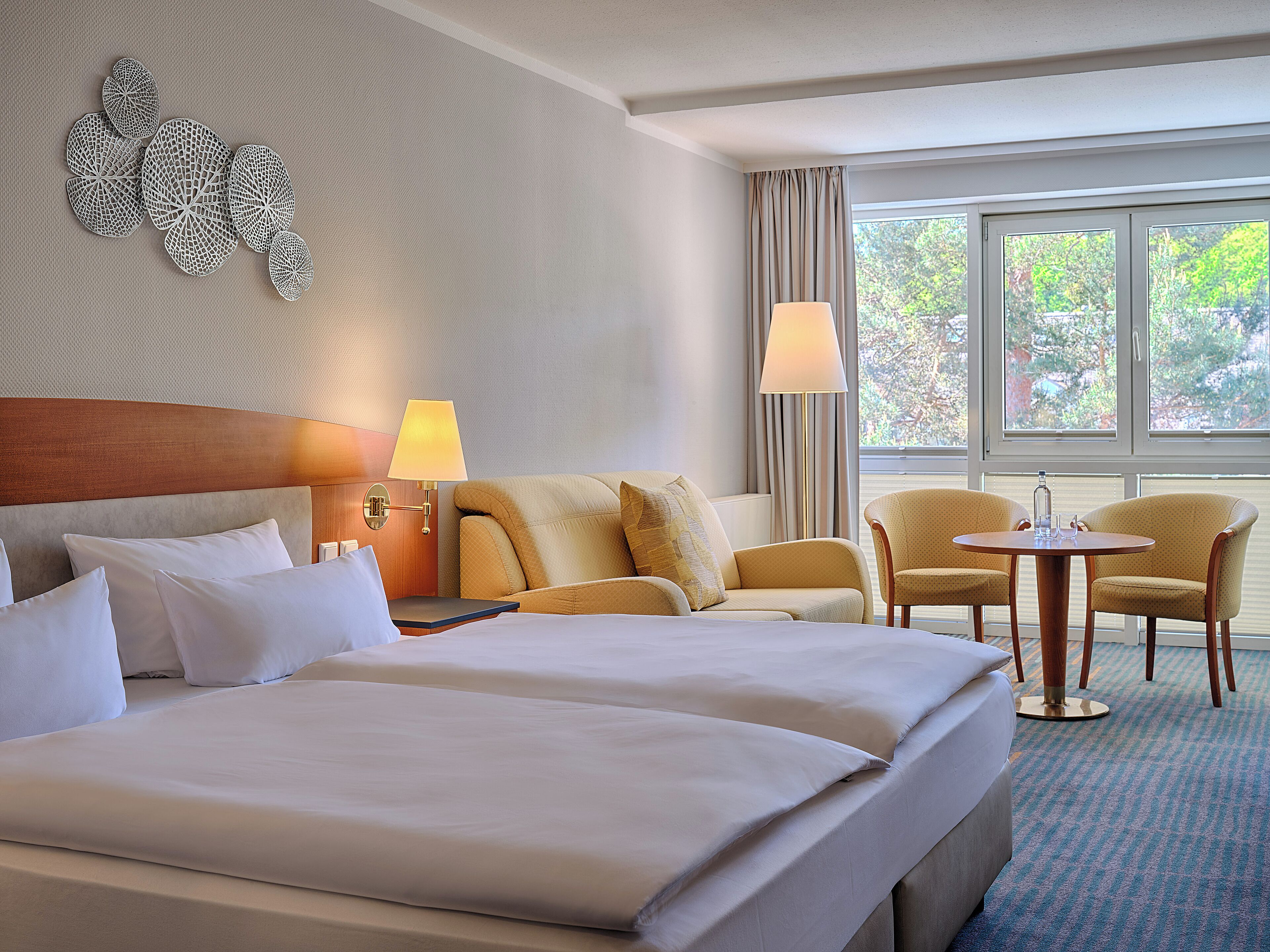Ein Hotelzimmer mit einem großen Bett, zwei Sesseln, einem kleinen Tisch und einem Fenster mit Vorhängen.