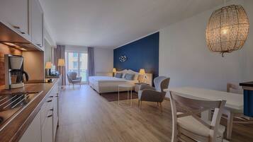 A modern hotel room with a kitchenette, a bed, a sofa, and a dining area.