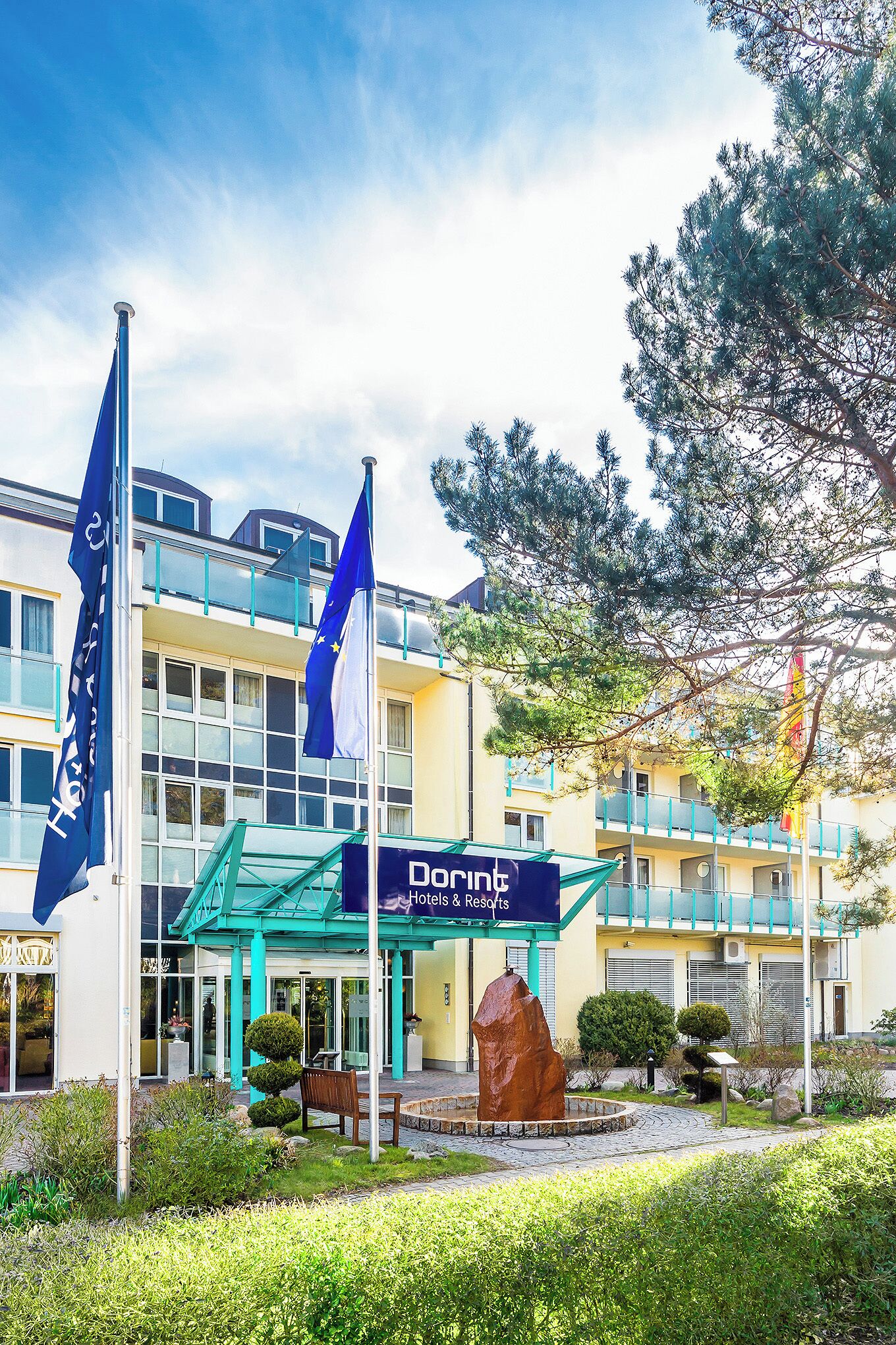 Entrada de un hotel con fachada de vidrio, un letrero que dice 'Dorne Hotels & Resorts' y dos banderas.