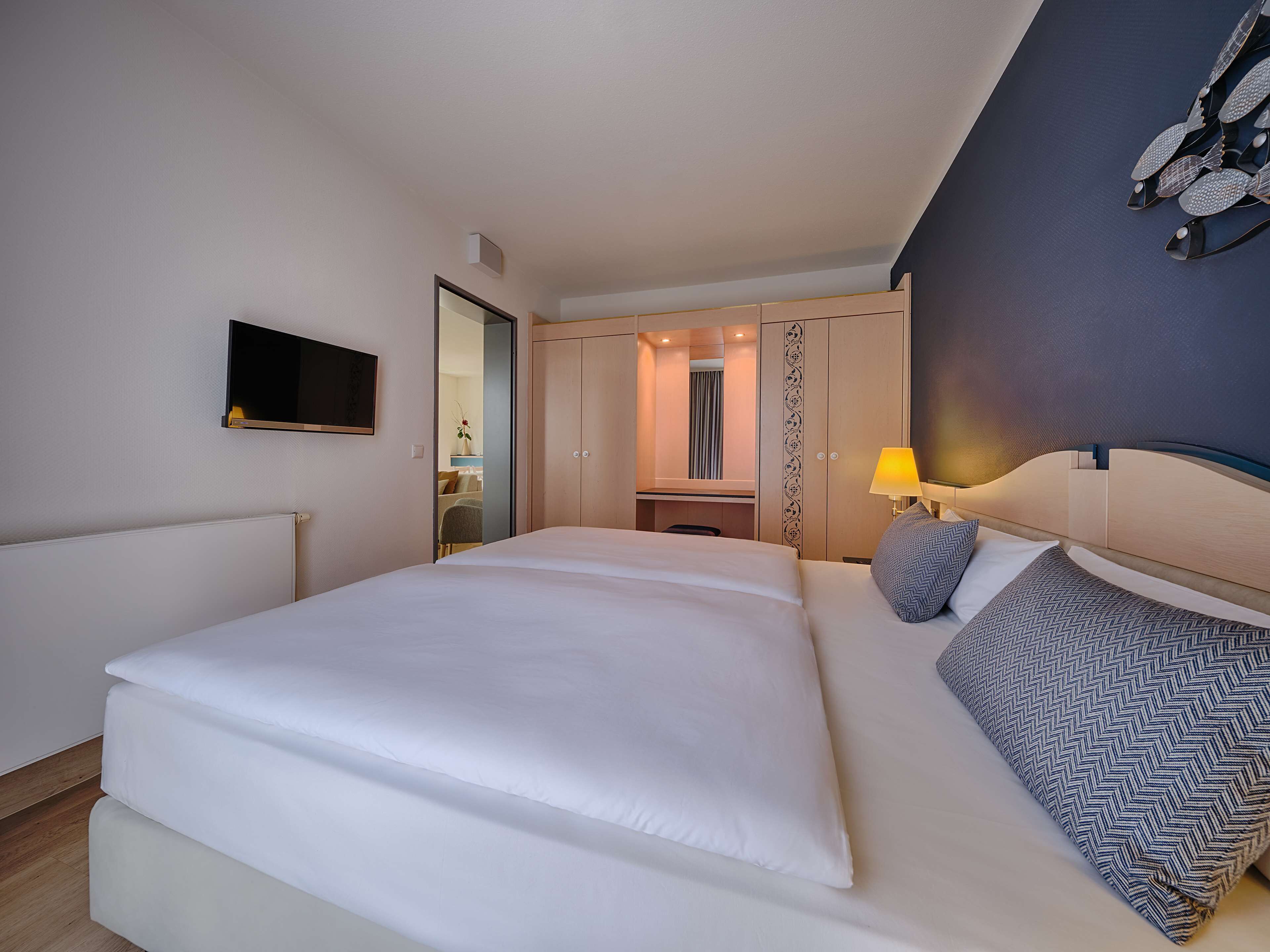 A modern hotel room with a large bed, a TV mounted on the wall, and a wardrobe with a mirror.