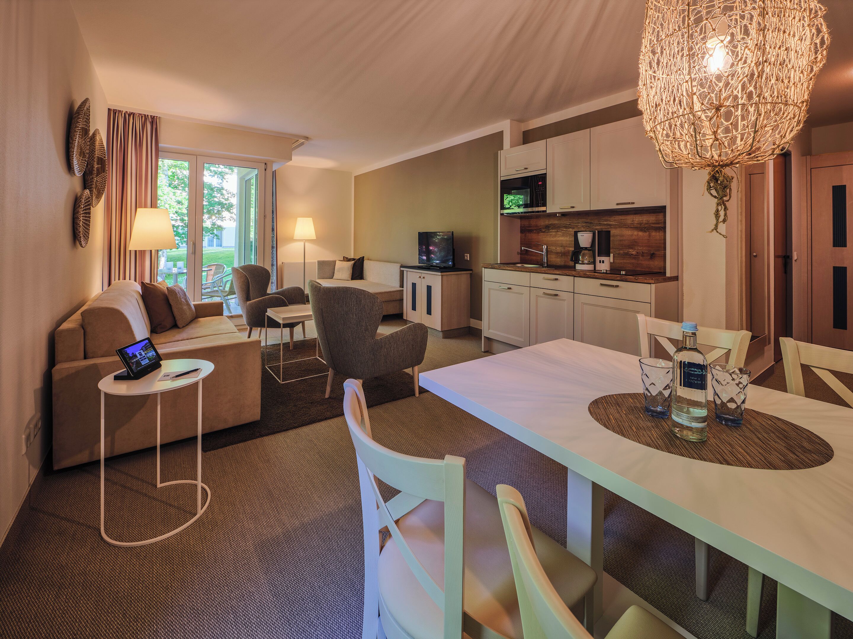 A modern hotel room with a dining area, kitchenette, and a large window.
