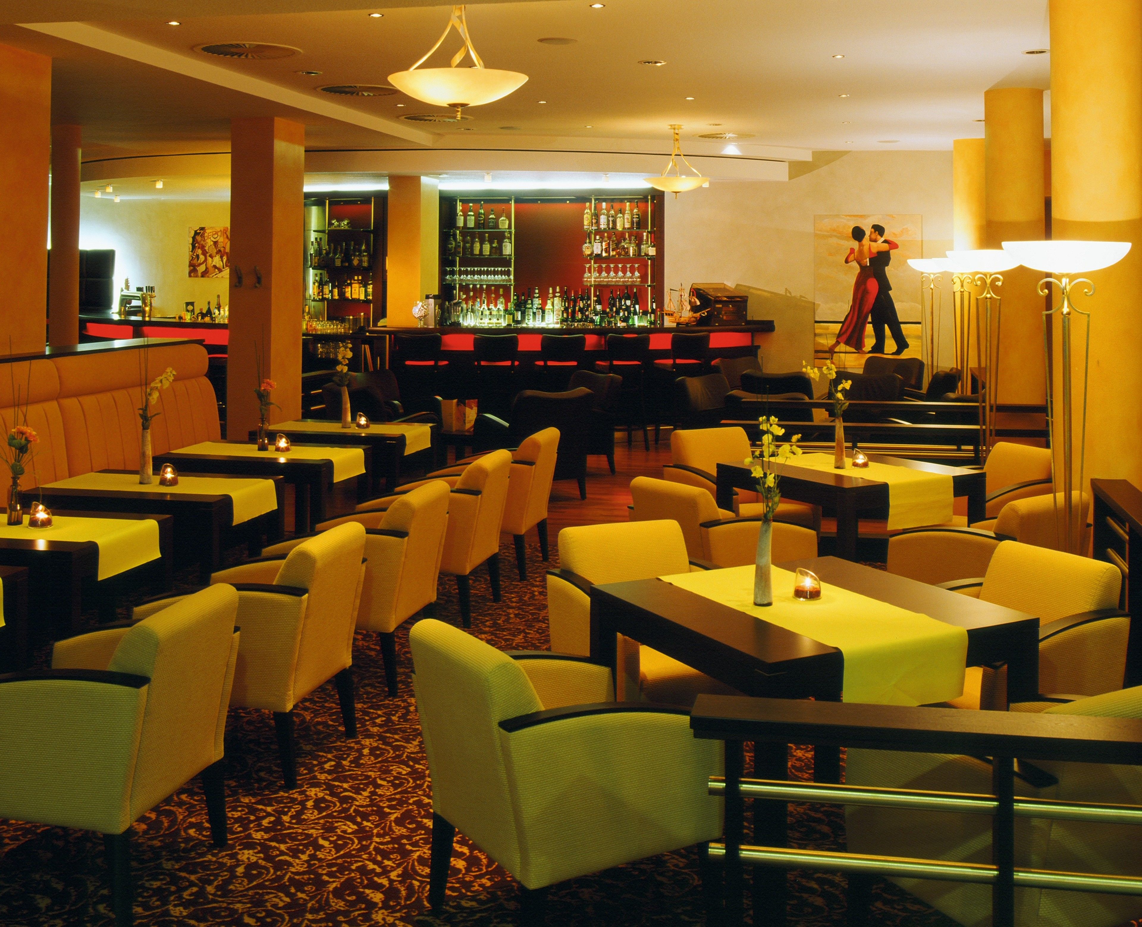 Ein Restaurant mit mehreren Tischen und Stühlen, einer Bar mit Regalen voller Flaschen, und eine Person im Hintergrund.