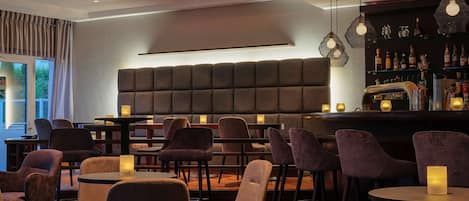 A modern bar area with cushioned seating, pendant lighting, and a bar stocked with bottles.
