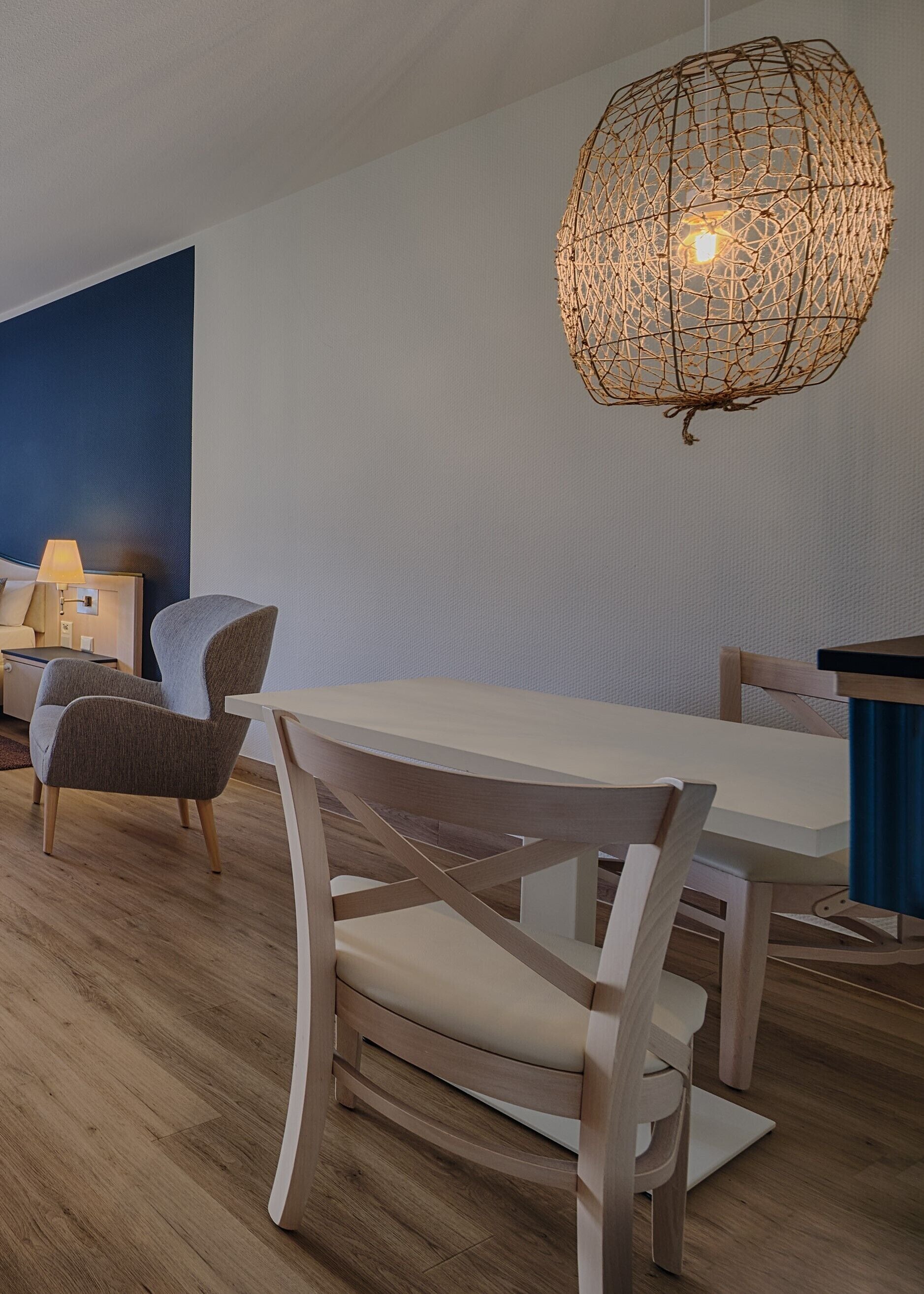 A modern dining area with a wooden table and chairs, a hanging woven light fixture, and a blue accent wall.