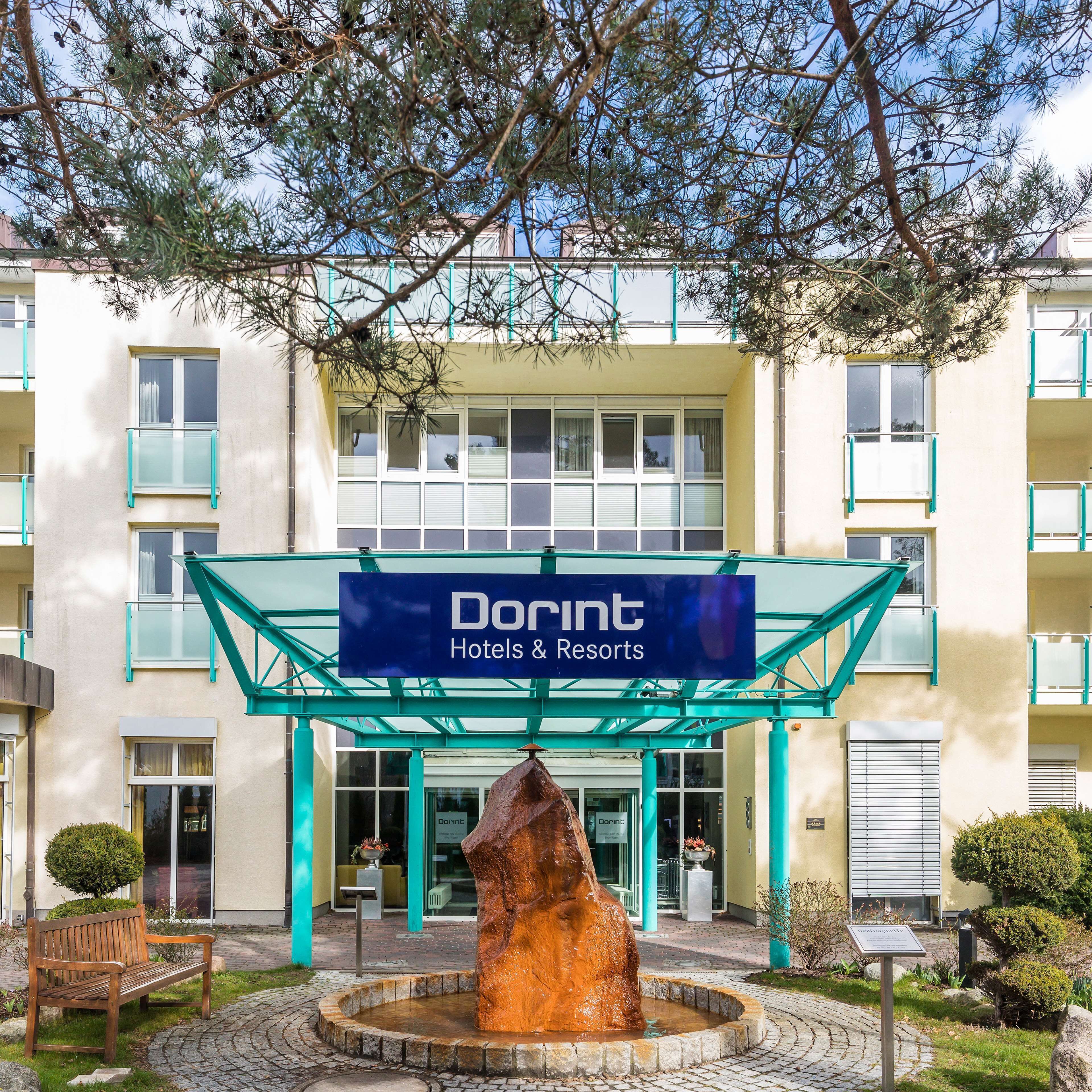 A Dorint Hotels & Resorts building with a central entrance, a stone fountain, and a bench in the foreground.