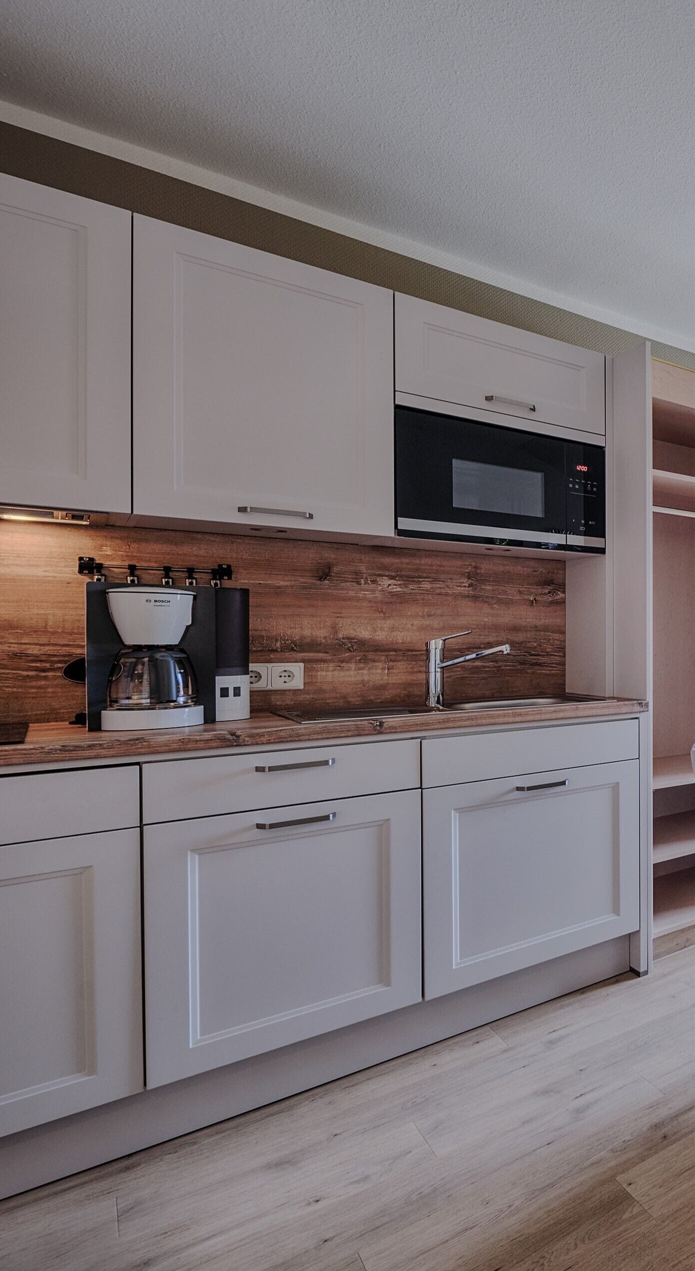 A modern kitchen with white cabinetry, a built-in microwave, and a coffee maker.