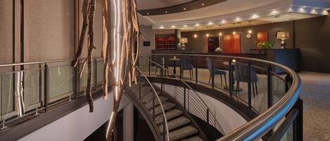 Un moderno vestíbulo de hotel con una escalera curva, un mostrador de recepción y una zona de estar.