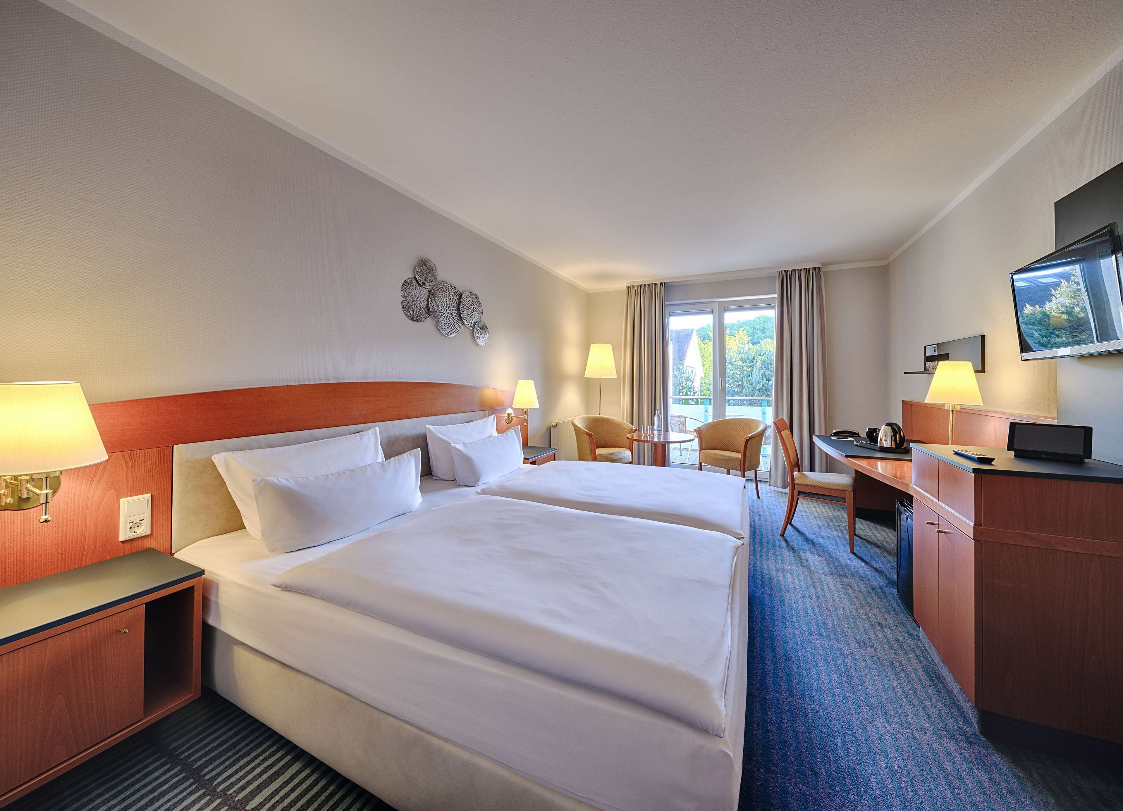A hotel room with two beds, a desk, a chair, a TV, and a balcony with curtains.