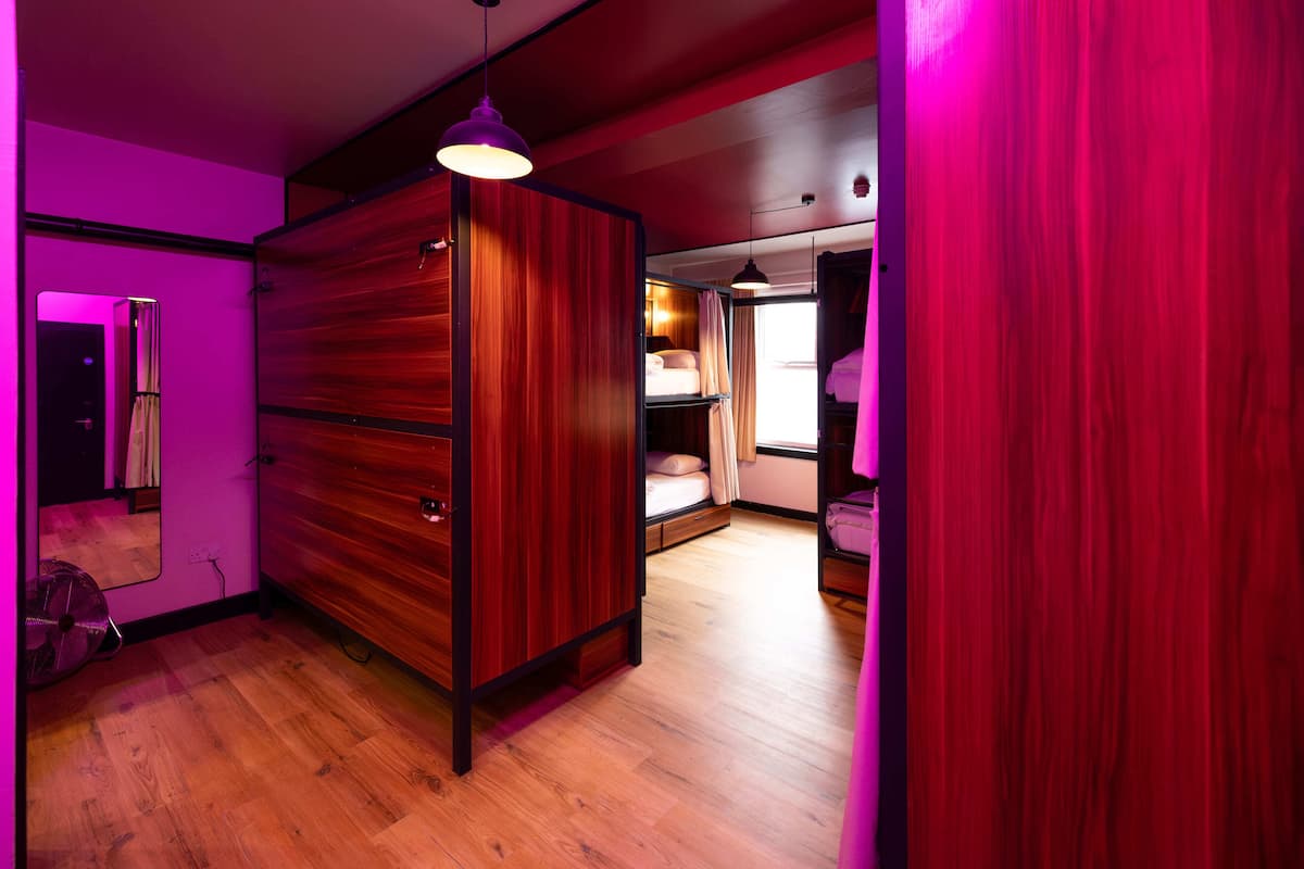 A room with a wooden wardrobe, a bed with a white duvet, and a window with curtains.