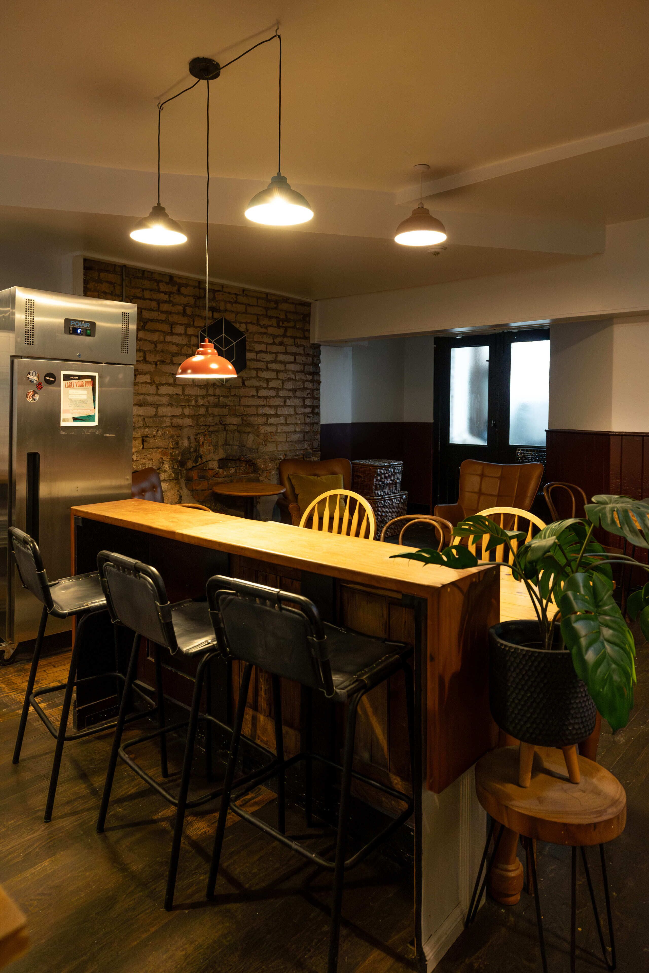 Une cuisine moderne avec un îlot central en bois, des tabourets de bar noirs, un réfrigérateur et des luminaires suspendus.