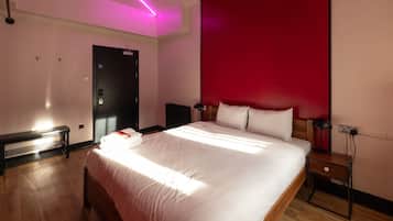 A modern hotel room with a large bed, a bedside table, a desk lamp, and a red accent wall.