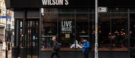 Un edificio con un cartel que dice "Wilson's Live Music Tonight" y un cartel que indica "Únete a nosotros para tomar cócteles".
